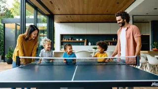 A modern, well-lit home with a family spanning three generations gathered around a ping pong table, smiling and engaged in play